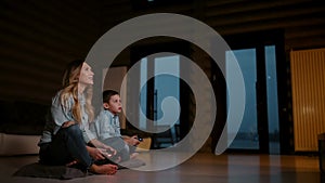 Beautiful mother with her son playing video games on gaming console in the living room of his house. Happy family in a