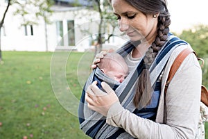 Beautiful mother with her son in sling, green nature