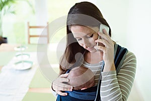 Beautiful mother with her son in sling and smartphone