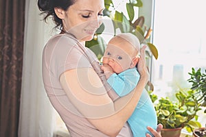 Beautiful mother holding in arms her little cute newborn infant son. Baby facial expressions.