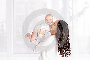 Beautiful mother holding a baby in her arms at the window of the house, the concept of a happy loving family, lifestyle