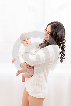 Beautiful mother holding a baby in her arms at the window of the house, the concept of a happy loving family, lifestyle