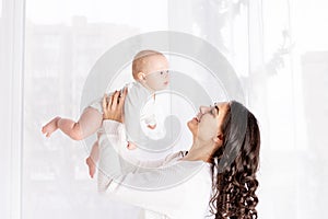 Beautiful mother holding a baby in her arms at the window of the house, the concept of a happy loving family, lifestyle