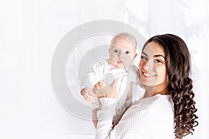 Beautiful mother holding a baby in her arms at the window of the house, the concept of a happy loving family, lifestyle