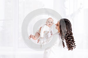 Beautiful mother holding a baby in her arms at the window of the house, the concept of a happy loving family, lifestyle