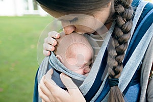 Beautiful mother kissing her son in sling, green nature