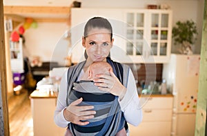 Beautiful mother in kitchen with her son sleeping in sling