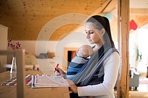 Beautiful mother in kitchen with her son sleeping in sling