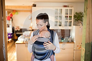 Beautiful mother in kitchen with her son sleeping in sling