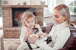 Beautiful mother, little daughter and a cat are sitting on the sofa near the fireplace. Family in the home interior. Cozy