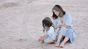 Beautiful mother and little daughter sitting on the beach