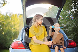 Beautiful mother and little son sit in trunk of car and blow soap bubbles. Photo about family travel