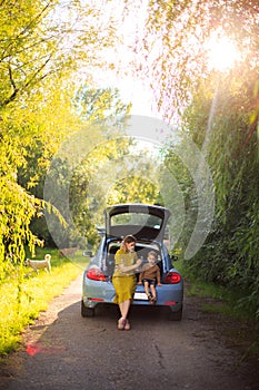 Beautiful mother and little son travelers sit in trunk of car on road and blow soap bubbles. Photo about family travel