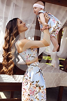 Beautiful mother with long dark hair posing with her little cute baby in similar dresses