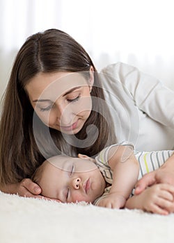 Beautiful mother looks at her 7 months old baby sleeping in the bed