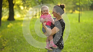 Beautiful mother playing with her daughter outdoors, woman holding her baby