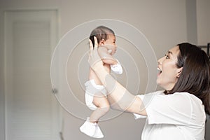 Beautiful mother is playing with her newborn baby in the bedroom