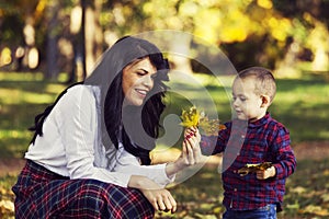 Beautiful mother plays with her son in the park in autumn
