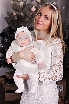Beautiful mother posing with her cute little baby girl beside Christmas tree
