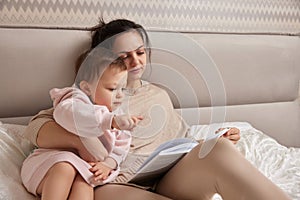 beautiful mother reading book to her cute little baby daughter