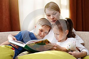 Beautiful mother is reading a book to her young children. Sister