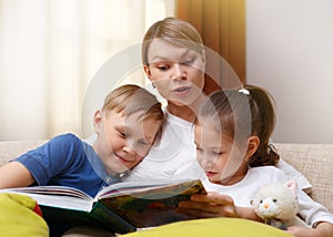 Beautiful mother is reading a book to her young children. Sister and brother is listening to a story.