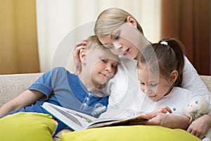 Beautiful mother is reading a book to her young children. Sister and brother is listening to a story.