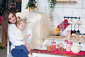 Beautiful mother with a small daughter in white sweaters sit in the kitchen and eat Christmas sweets. cozy photo in a stylish