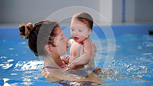 Beautiful mother teaching cute baby girl how to swim in a swimming pool. Child having fun in water with mom.