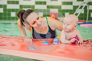 Beautiful mother teaching cute baby girl how to swim in a swimming pool. Child having fun in water with mom