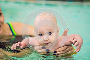 Beautiful mother teaching cute baby girl how to swim in a swimming pool. Child having fun in water with mom