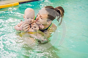 Beautiful mother teaching cute baby girl how to swim in a swimming pool. Child having fun in water with mom