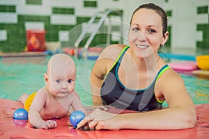 Beautiful mother teaching cute baby girl how to swim in a swimming pool. Child having fun in water with mom