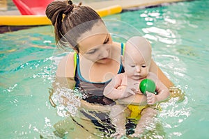 Beautiful mother teaching cute baby girl how to swim in a swimming pool. Child having fun in water with mom