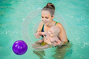 Beautiful mother teaching cute baby girl how to swim in a swimming pool. Child having fun in water with mom