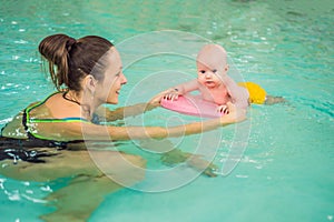 Beautiful mother teaching cute baby girl how to swim in a swimming pool. Child having fun in water with mom