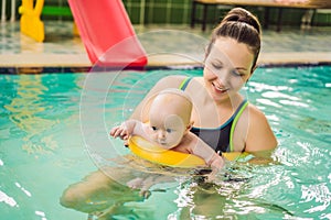 Beautiful mother teaching cute baby girl how to swim in a swimming pool. Child having fun in water with mom