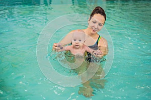 Beautiful mother teaching cute baby girl how to swim in a swimming pool. Child having fun in water with mom