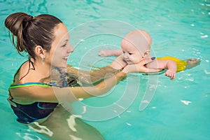 Beautiful mother teaching cute baby girl how to swim in a swimming pool. Child having fun in water with mom