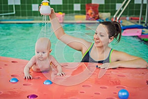 Beautiful mother teaching cute baby girl how to swim in a swimming pool. Child having fun in water with mom