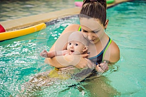 Beautiful mother teaching cute baby girl how to swim in a swimming pool. Child having fun in water with mom