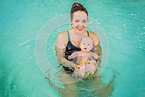 Beautiful mother teaching cute baby girl how to swim in a swimming pool. Child having fun in water with mom