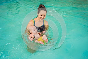 Beautiful mother teaching cute baby girl how to swim in a swimming pool. Child having fun in water with mom