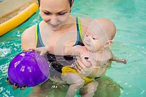 Beautiful mother teaching cute baby girl how to swim in a swimming pool. Child having fun in water with mom