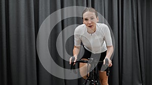 Beautiful motivated female cycling out of saddle on smart home indoor cycle trainer wearing white outfit. Indoor cardio training c