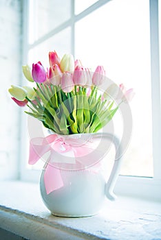 Beautiful motley tulips in a white vase against the window.