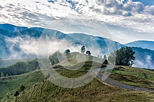 Beautiful mountain landscape of a foggy morning with and old house, trees and clouds