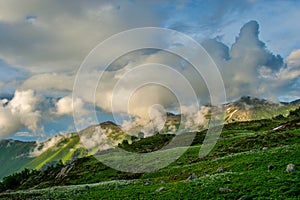 Beautiful mountain landscape with green slopes and snow and clouds