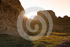 Beautiful mountain landscape - rough big boulders on lush green grass meadow in bright golden orange sunset sunlight with rays