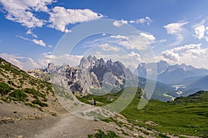 beautiful mountain landscape with sharp edges, green meadows and tourists on the trail. Italian Dolomites